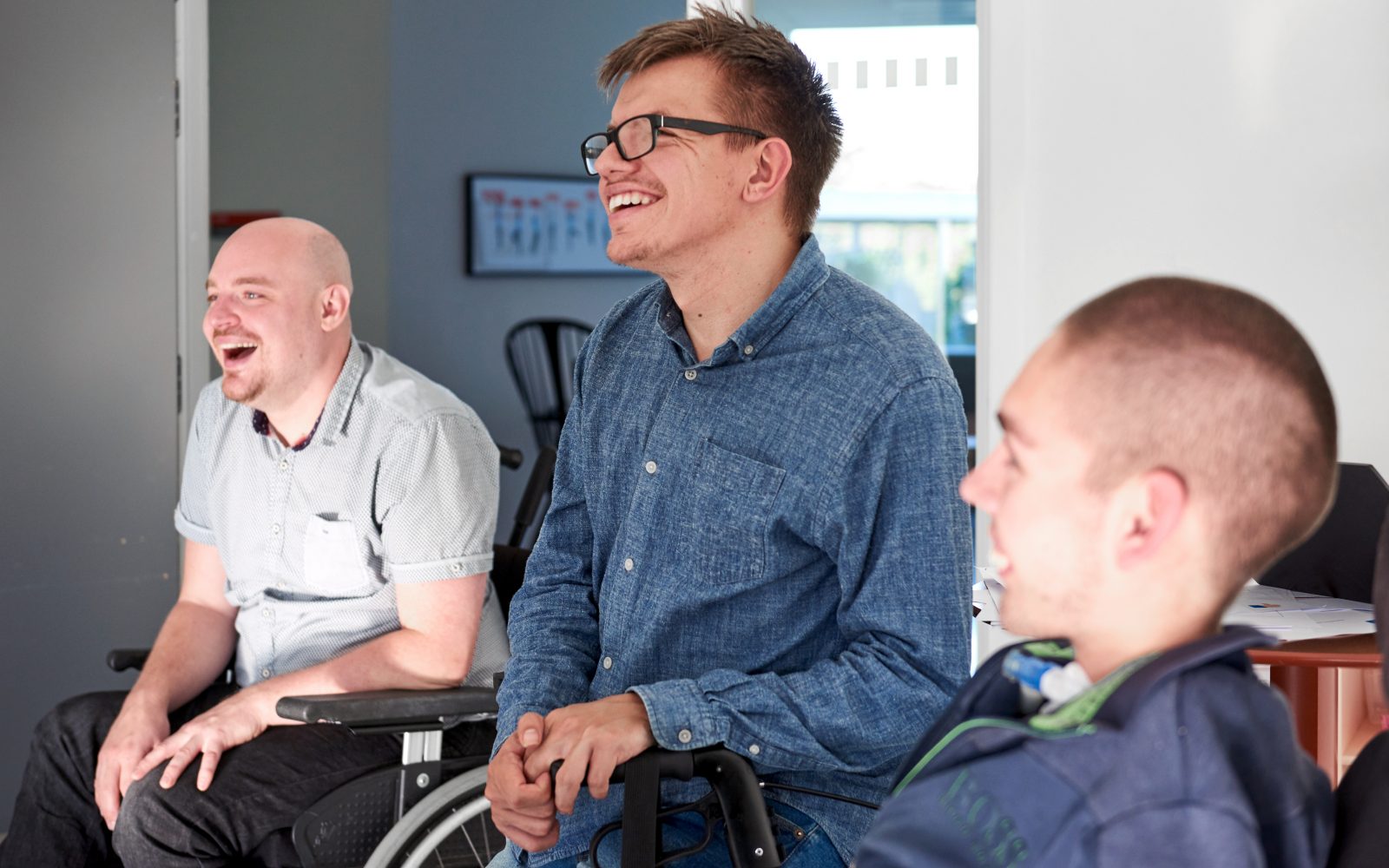 Tre unge mænd sidder med siden til og griner af noget uden for billedet