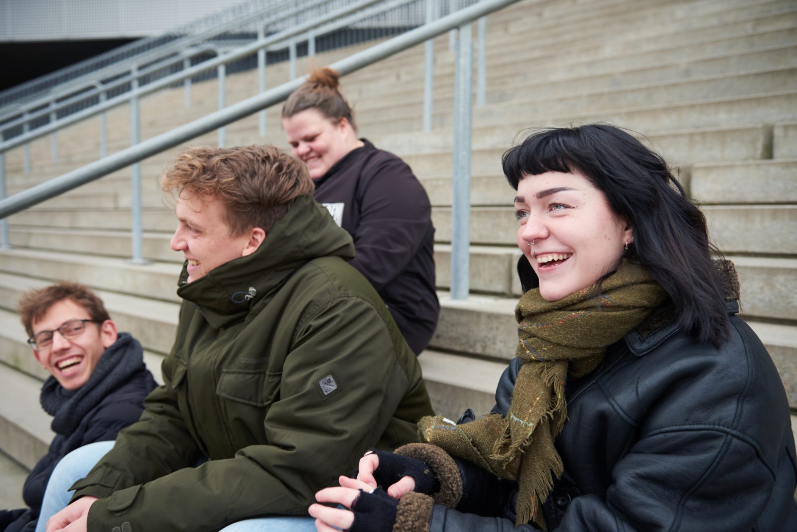 Fire unge sidder på en trappe og snakker sammen og smiler