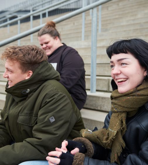 Fire unge sidder på en trappe og snakker sammen og smiler