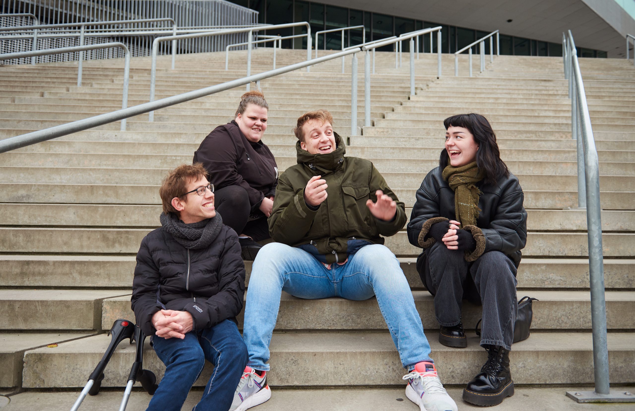 Fire unge sidder på en trappe og snakker sammen og smiler