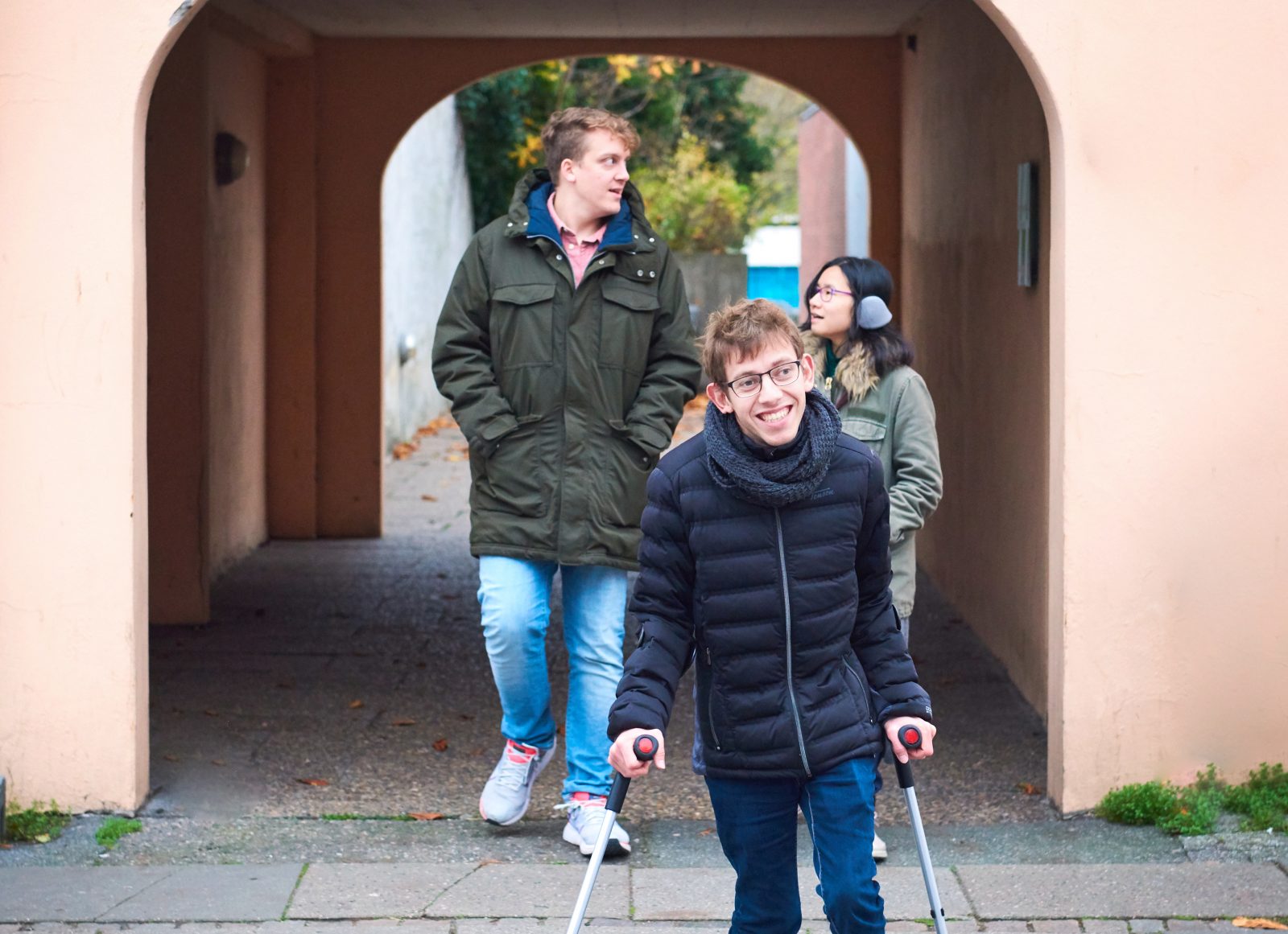 Tre unge frivillige i SUMH går sammen på gaden, en har krykker.
