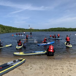Unge med redningsveste på SUP-boards ved en sø.