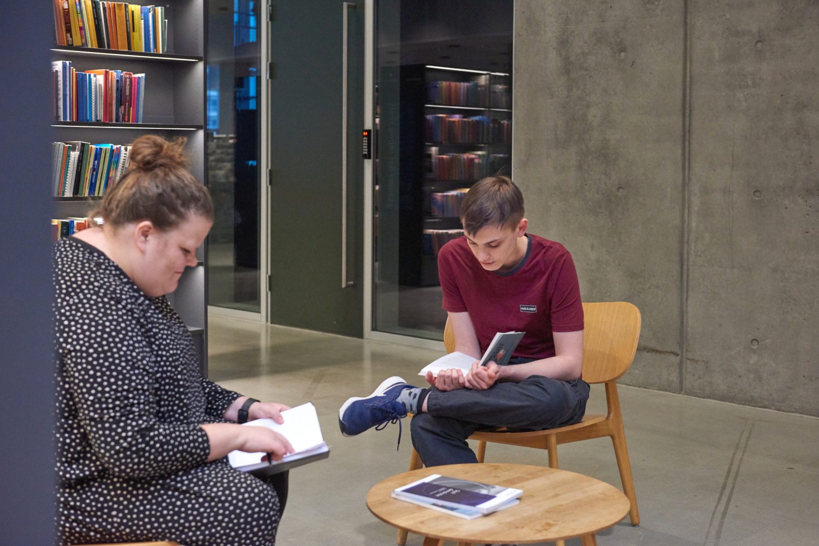 To personer sidder i et bibliotek og læser i hver deres bog.
